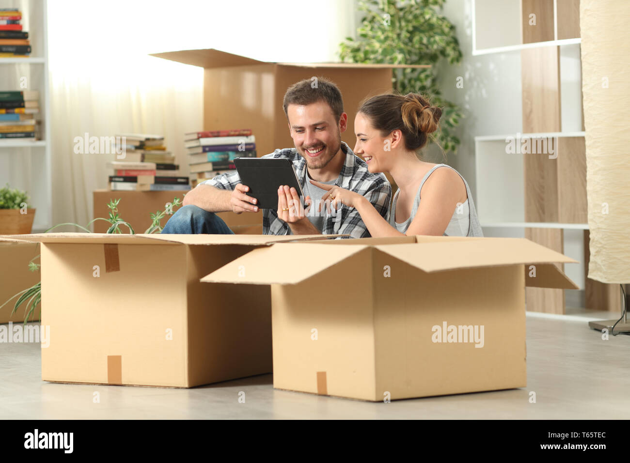 Glückliches Paar Umzug prüfen Tablette Inhalt sitzen auf dem Boden Stockfoto