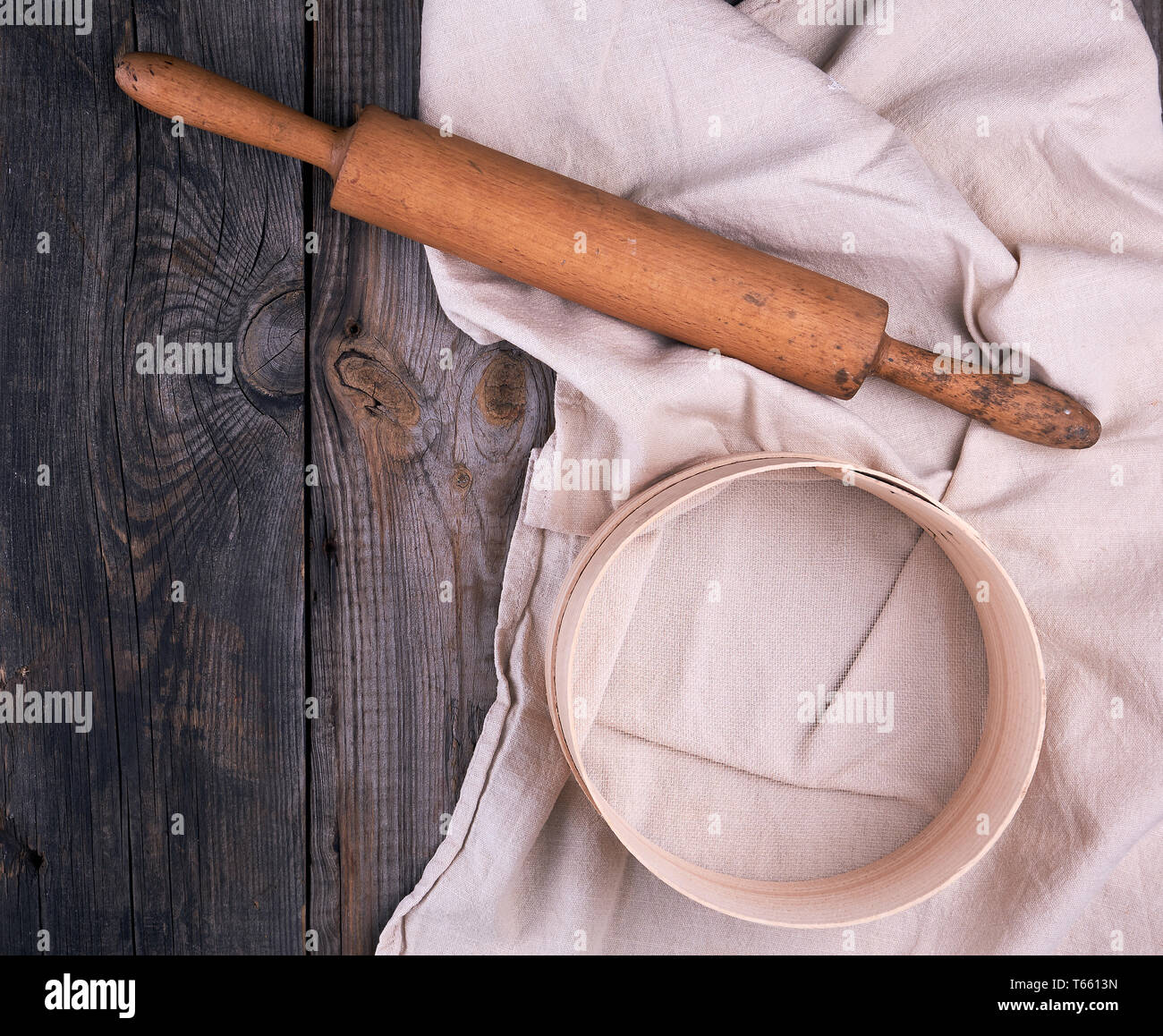 Alte hölzerne Rolling Pin auf ein Textil Serviette mit Stickerei und eine runde Sieb für Mehl, grau Holz- Hintergrund Stockfoto