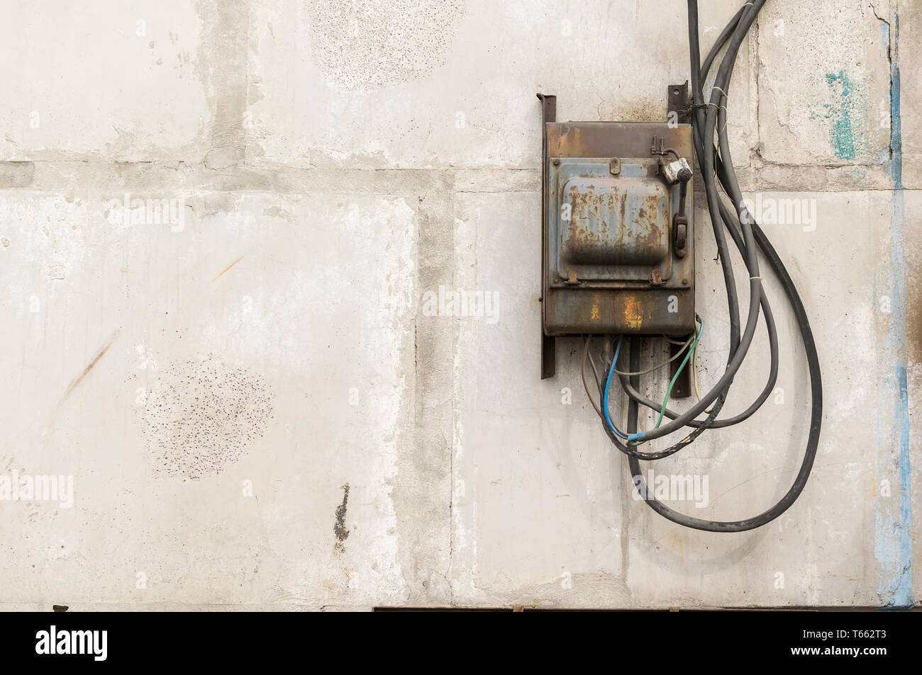 Alten rostigen ungepflegt elektrische Abschirmung mit einem Schalter an der Wand eines industriellen Gebäude aus Beton Bausteine mit geschmolzene Drähte festsitzen heraus Stockfoto
