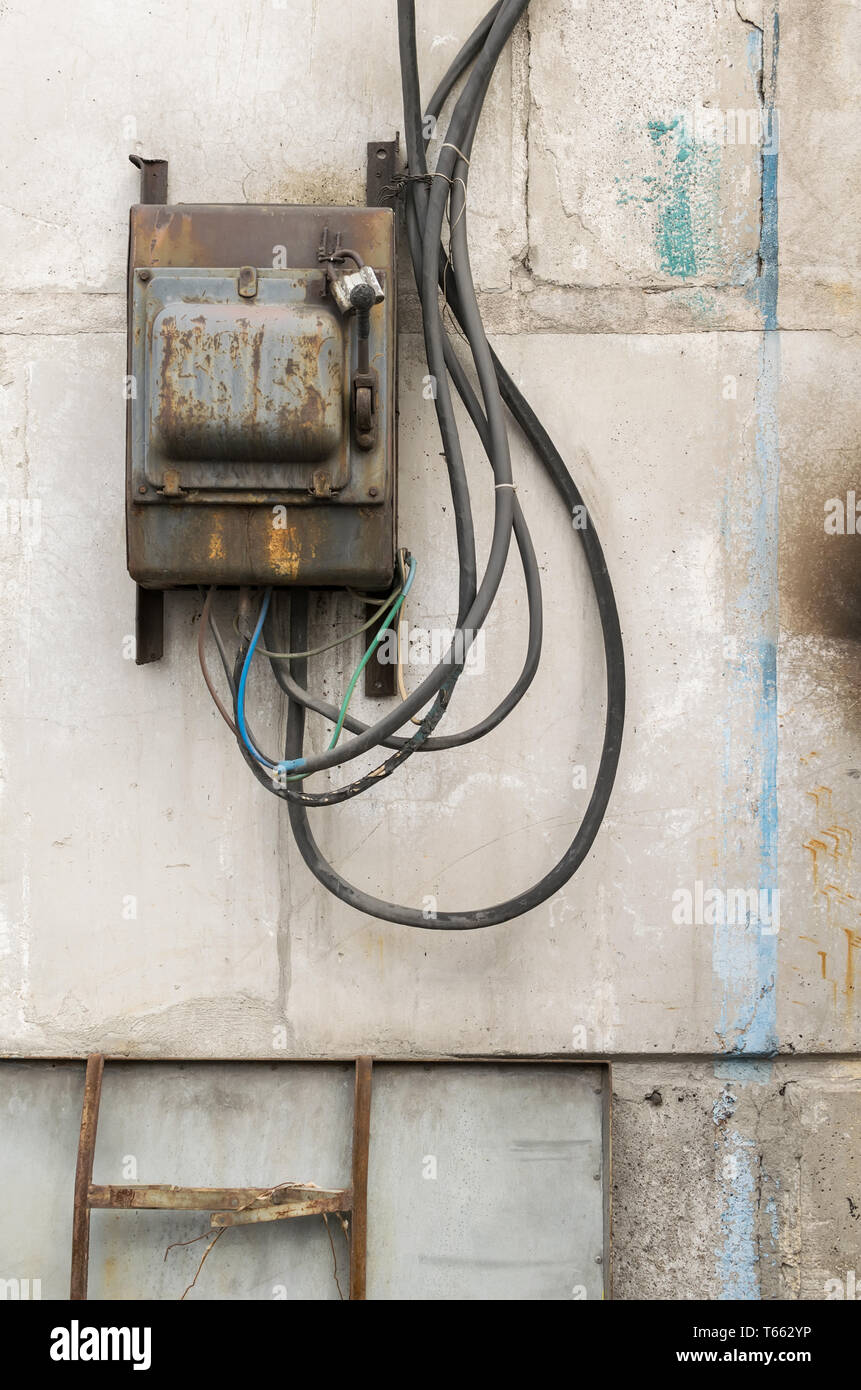 Alten rostigen ungepflegt elektrische Abschirmung mit einem Schalter an der Wand eines industriellen Gebäude aus Beton Bausteine mit geschmolzene Drähte festsitzen heraus Stockfoto