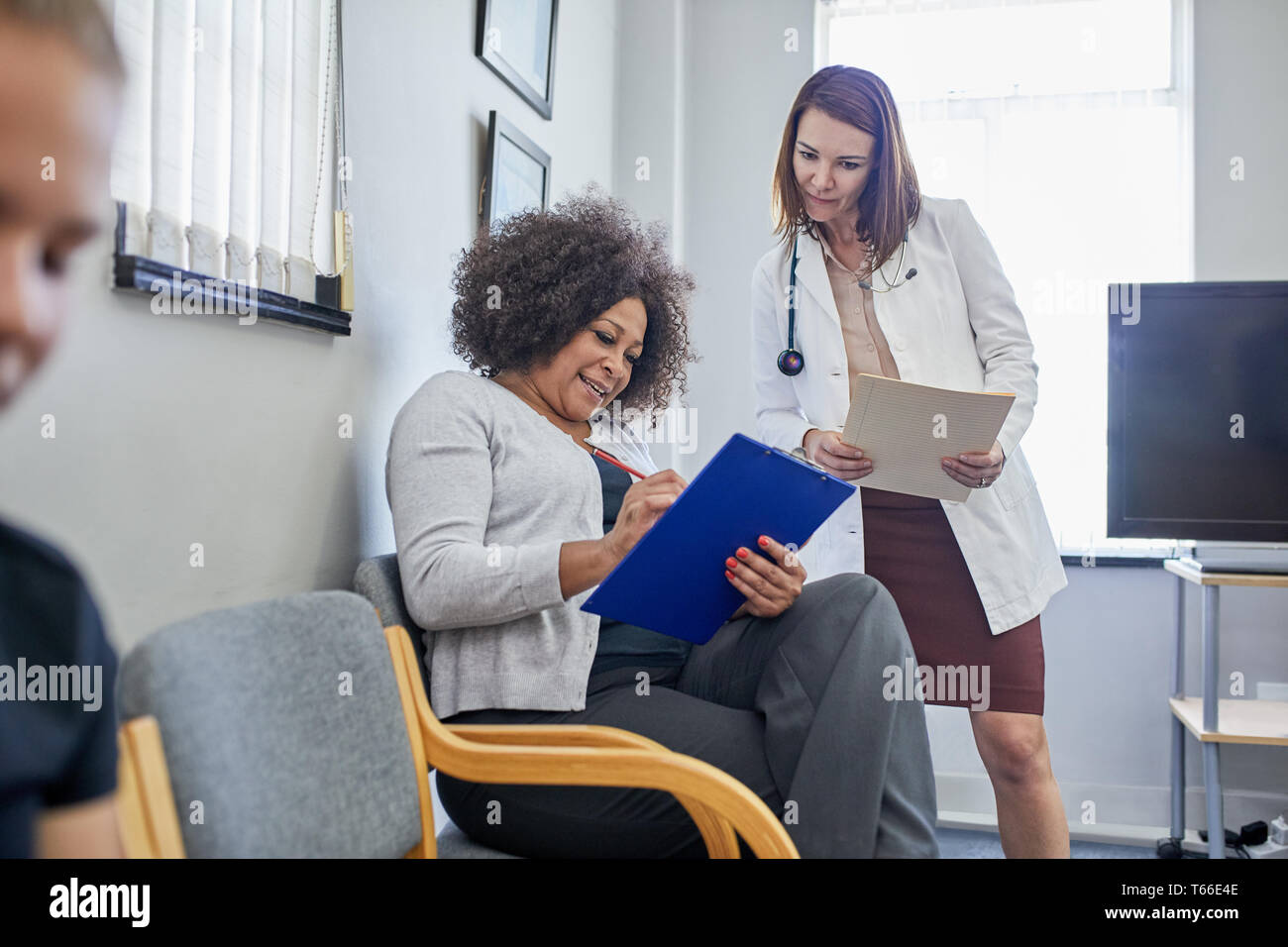 Weibliche Arzt und Patient diskutieren Schreibarbeit in Klinik Wartezimmer Stockfoto