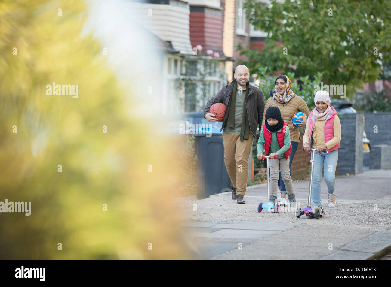 Muslimische Familie Wandern und Reiten Roller auf Nachbarschaft Bürgersteig Stockfoto