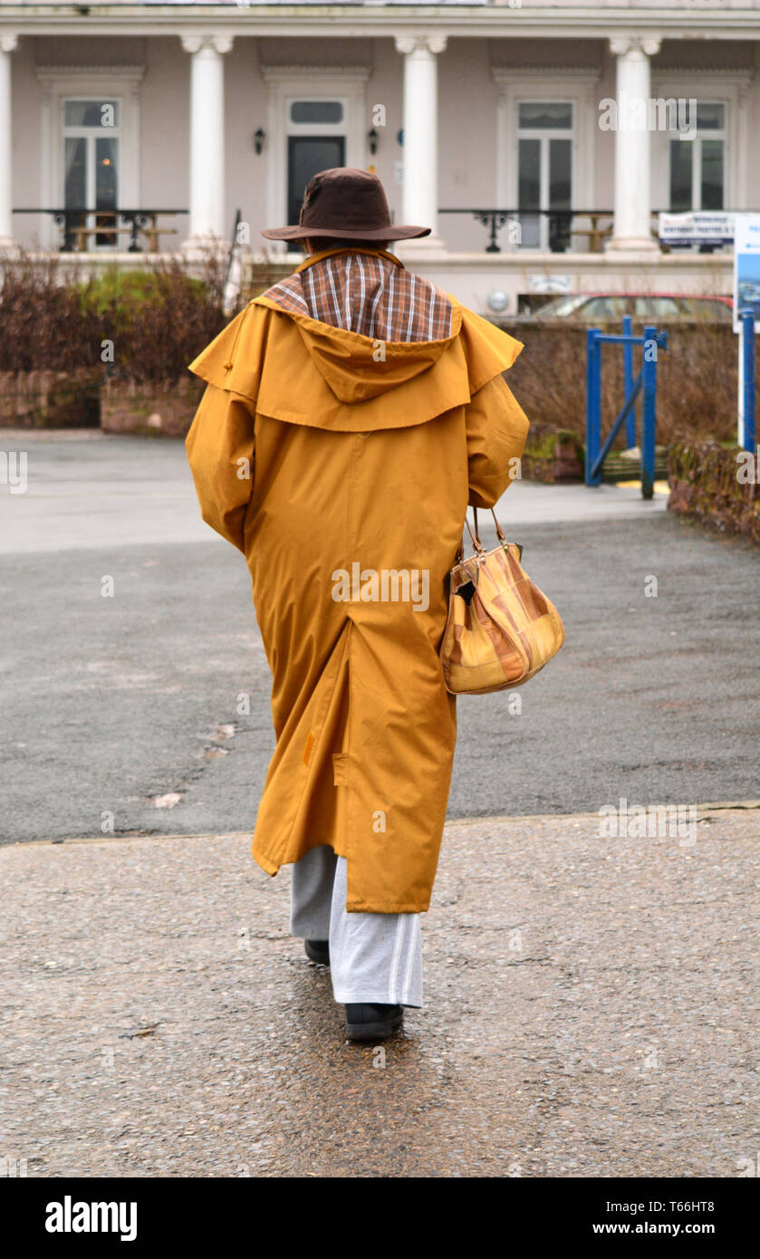 Rückansicht der Frau in der Kapuze Regenmantel und Sonnenhut mit Stockfoto