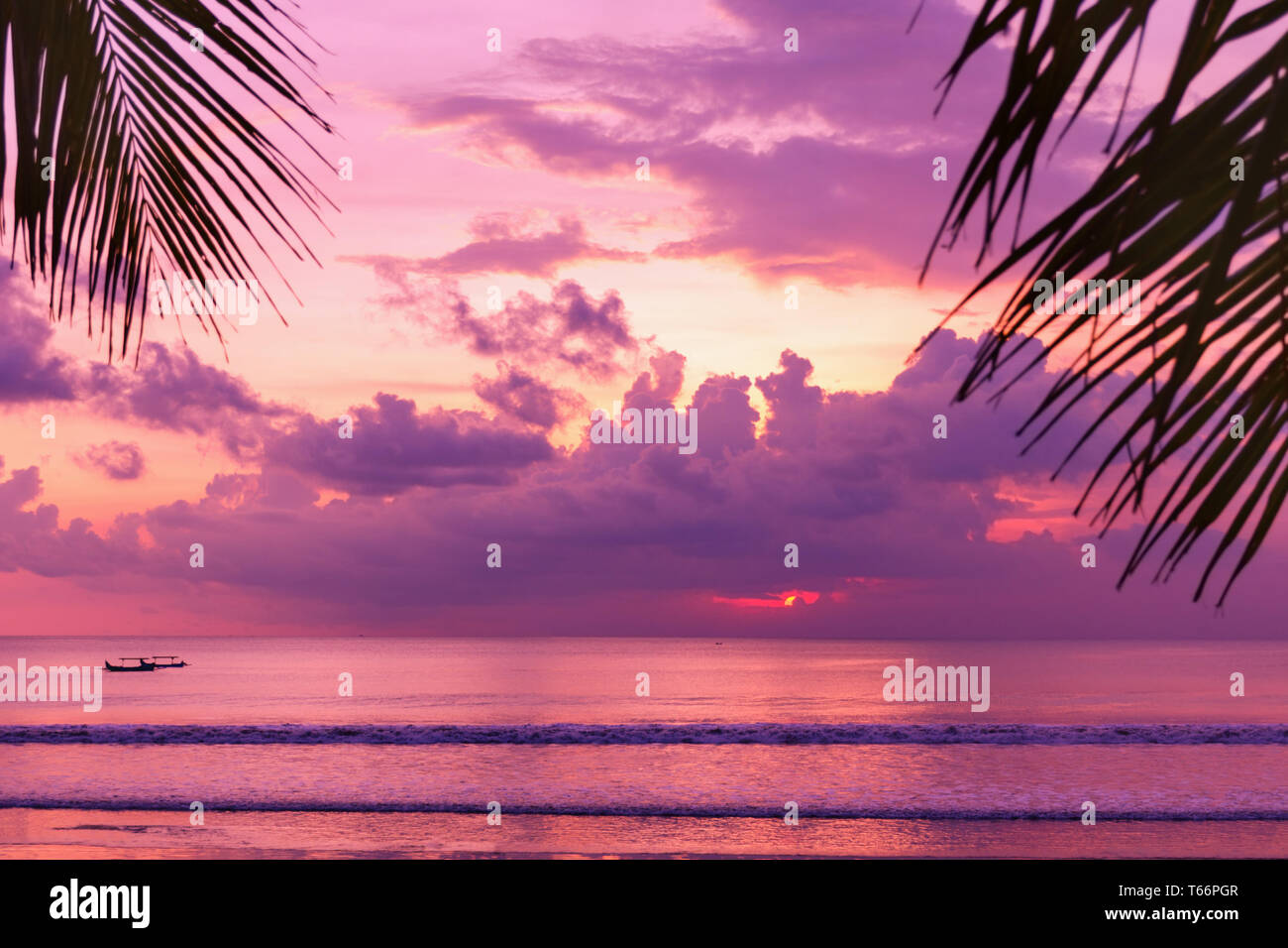 Lila Sonnenuntergang am Strand. Blick auf das Ufer durch Palmblätter. Fantastisch bunte Landschaft. Malerische Ansicht. Farbe in der Natur. Bali, Kuta. Stockfoto