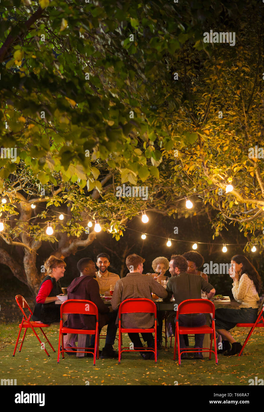 Freunde genießen das Abendessen Garden Party unter Bäume mit Lichterketten Stockfoto