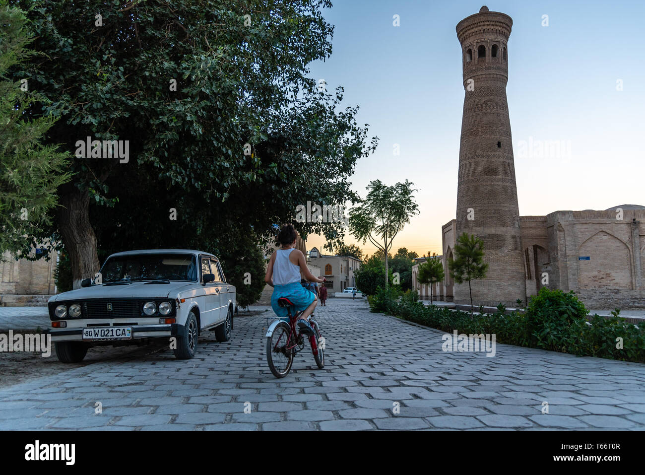 Ein Mädchen reiten ihr Fahrrad um eine sowjetische Ära Auto in Buchara, Usbekistan Stockfoto
