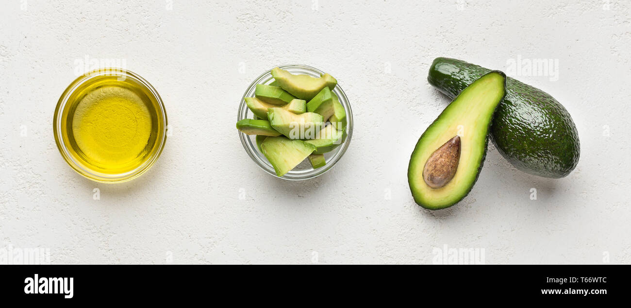 Ganze und aufgeschnittene Avocados und Öl in Schalen auf konkreten Hintergrund der Ansicht von oben. Vegane Ernährung Konzept Stockfoto