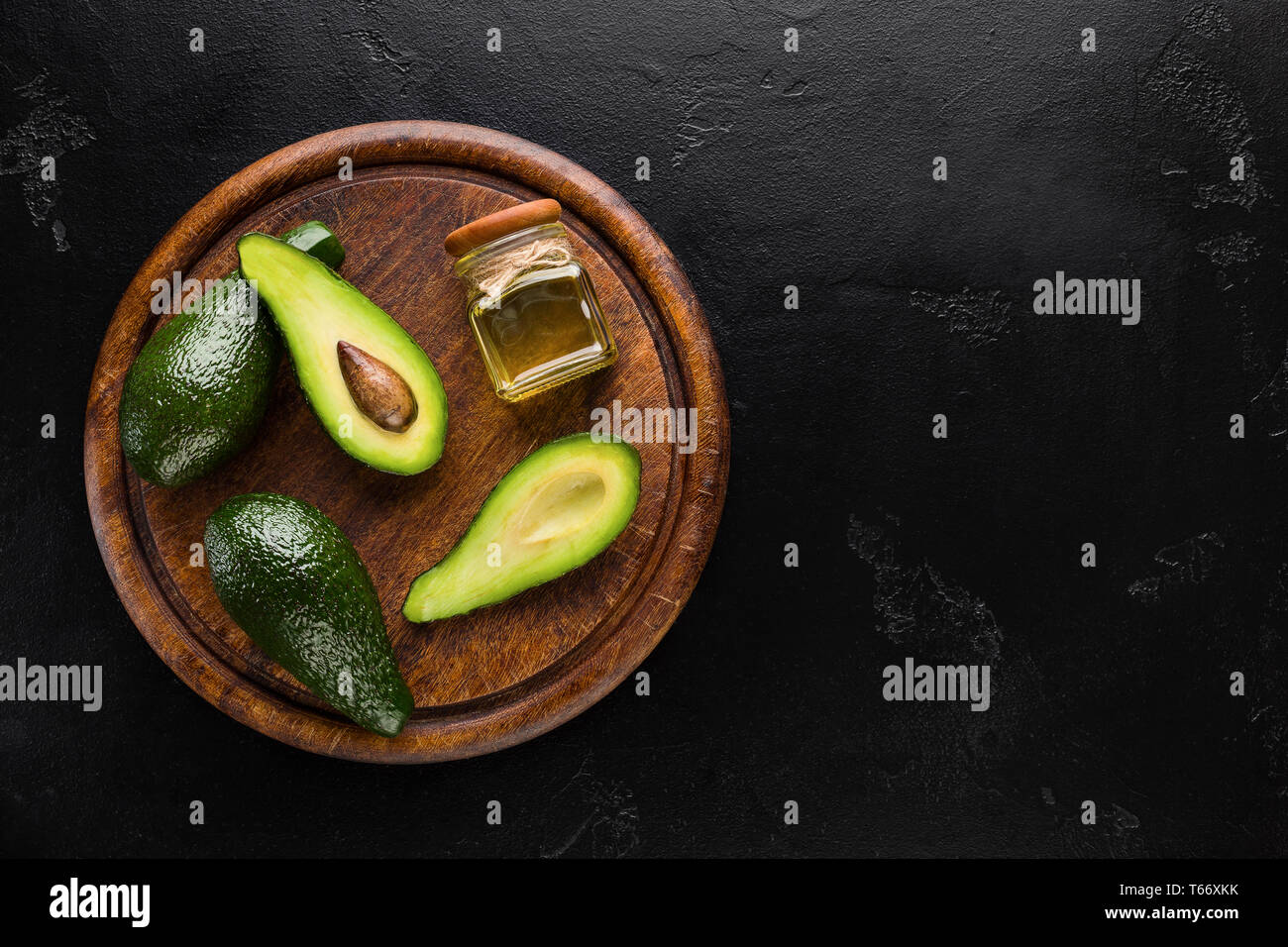 In Scheiben geschnitten und ganze Avocados und eine Flasche Öl auf Holzplatte auf schwarzem Hintergrund oben anzeigen, kopieren. Gesunde Ernährung Konzept Stockfoto