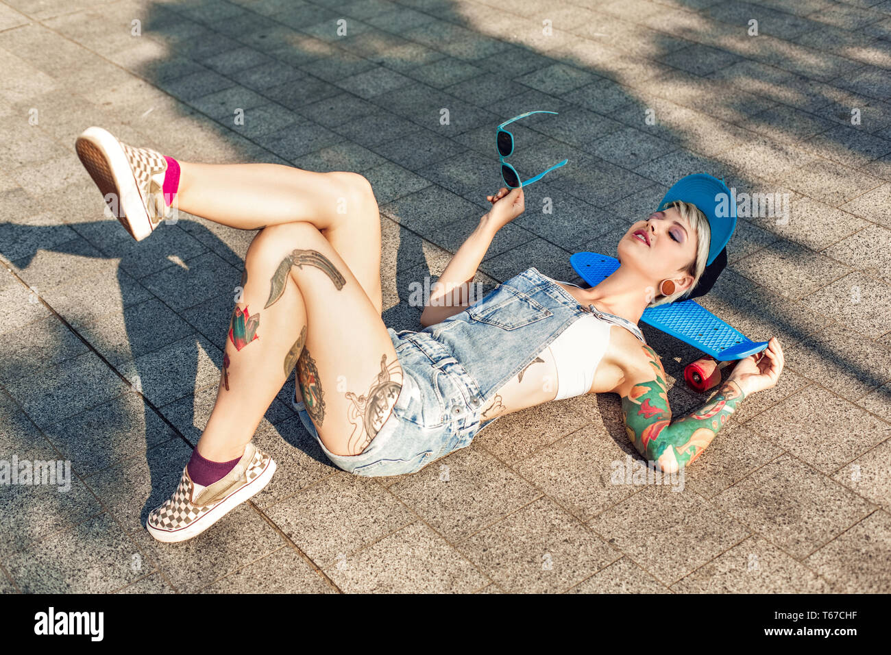 Junge alternative Mädchen skater tragen Cap liegen auf der Straße Kopf auf Penny board Holding Sonnenbrille geschlossenen Augen lächeln entspannt Stockfoto