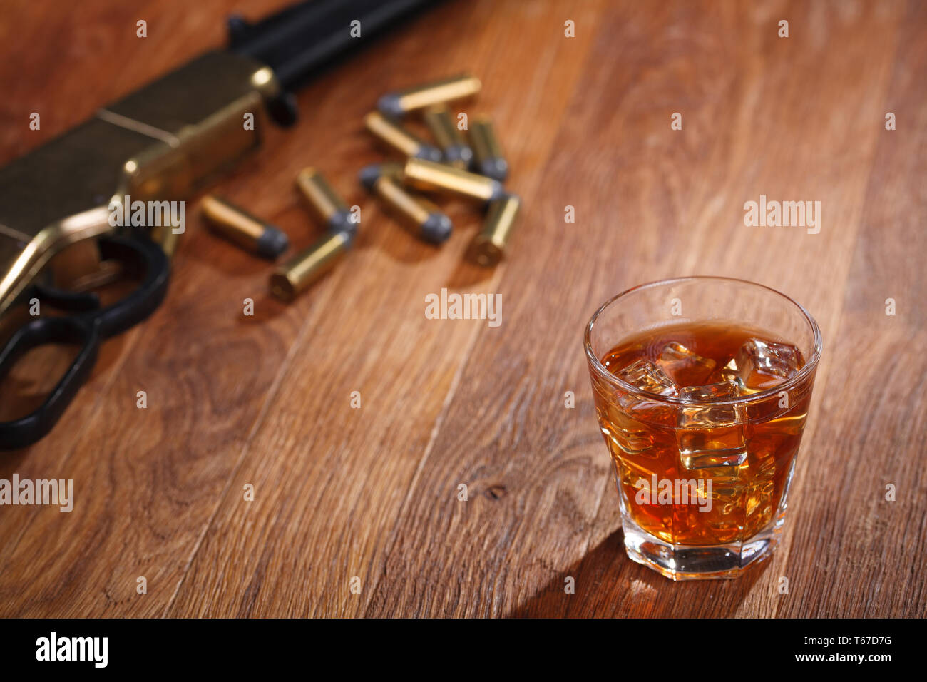 Wild West Gewehr und Munition mit Glas mit Whiskey und Eis auf Bar aus Holz Tisch Stockfoto