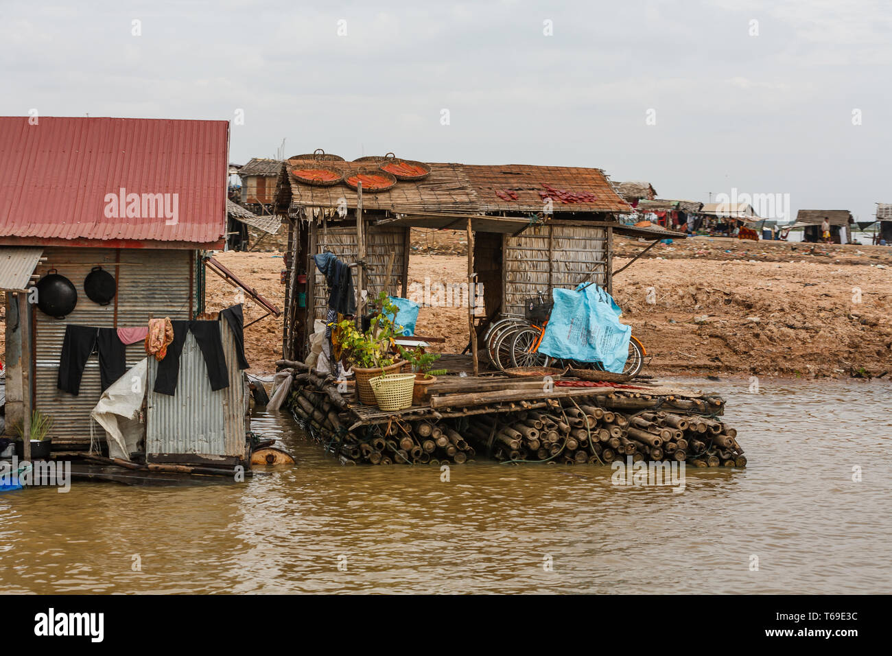 Ein schwimmendes Dorfhaus in Kambodscha, gebaut auf Bambusflößen, mit Kleidung hängen draußen und Fahrrädern, die mit blauen Planen bedeckt sind. Stockfoto