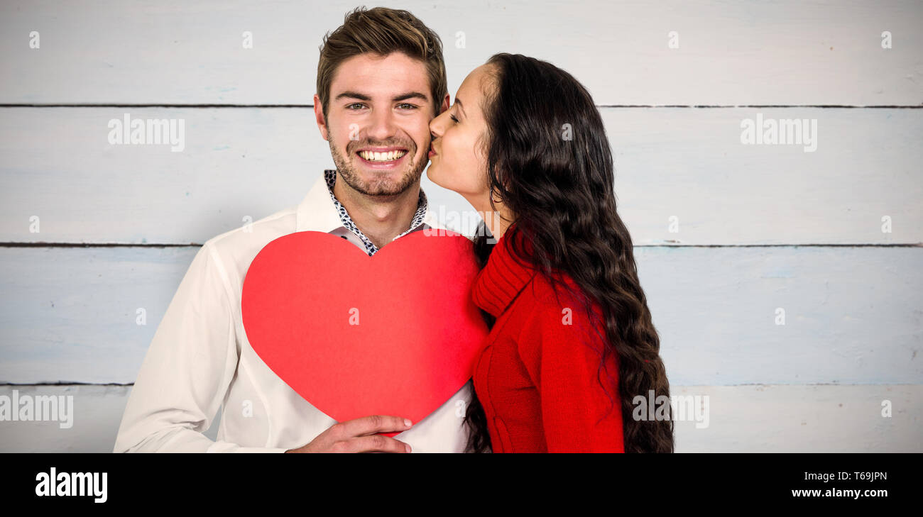 Zusammengesetztes Bild des Mannes halten Papierherz und wird von Freundin geküsst Stockfoto