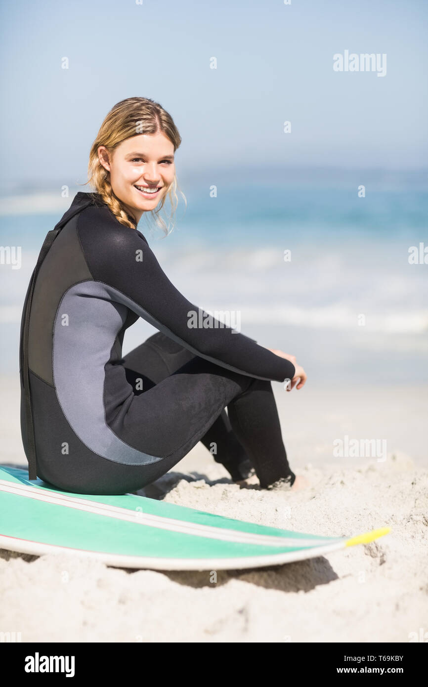 Porträt der Frau im Neoprenanzug mit Surfbrett am Strand sitzen Stockfoto