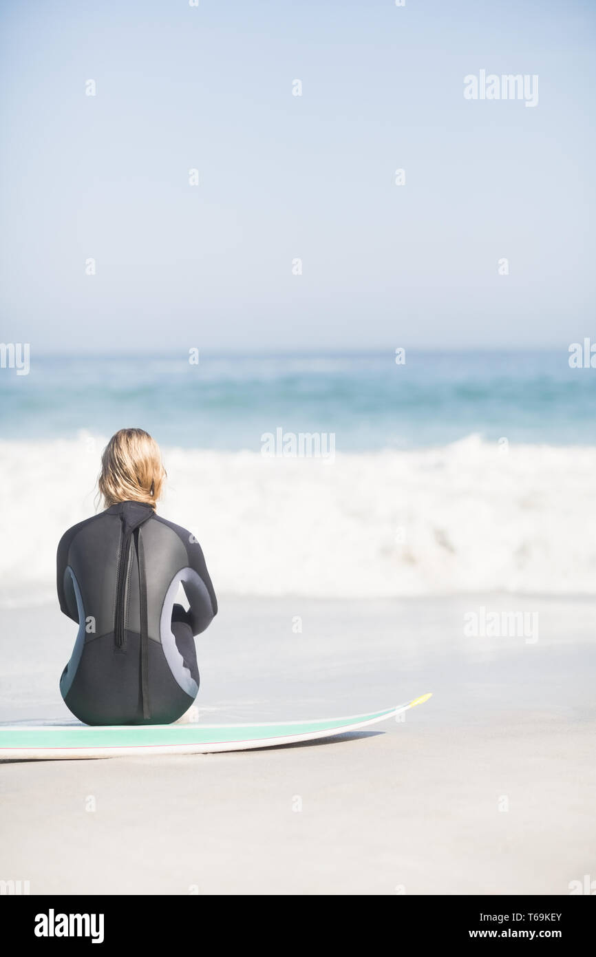 Rückansicht der Frau im Neoprenanzug mit Surfbrett am Strand sitzen Stockfoto