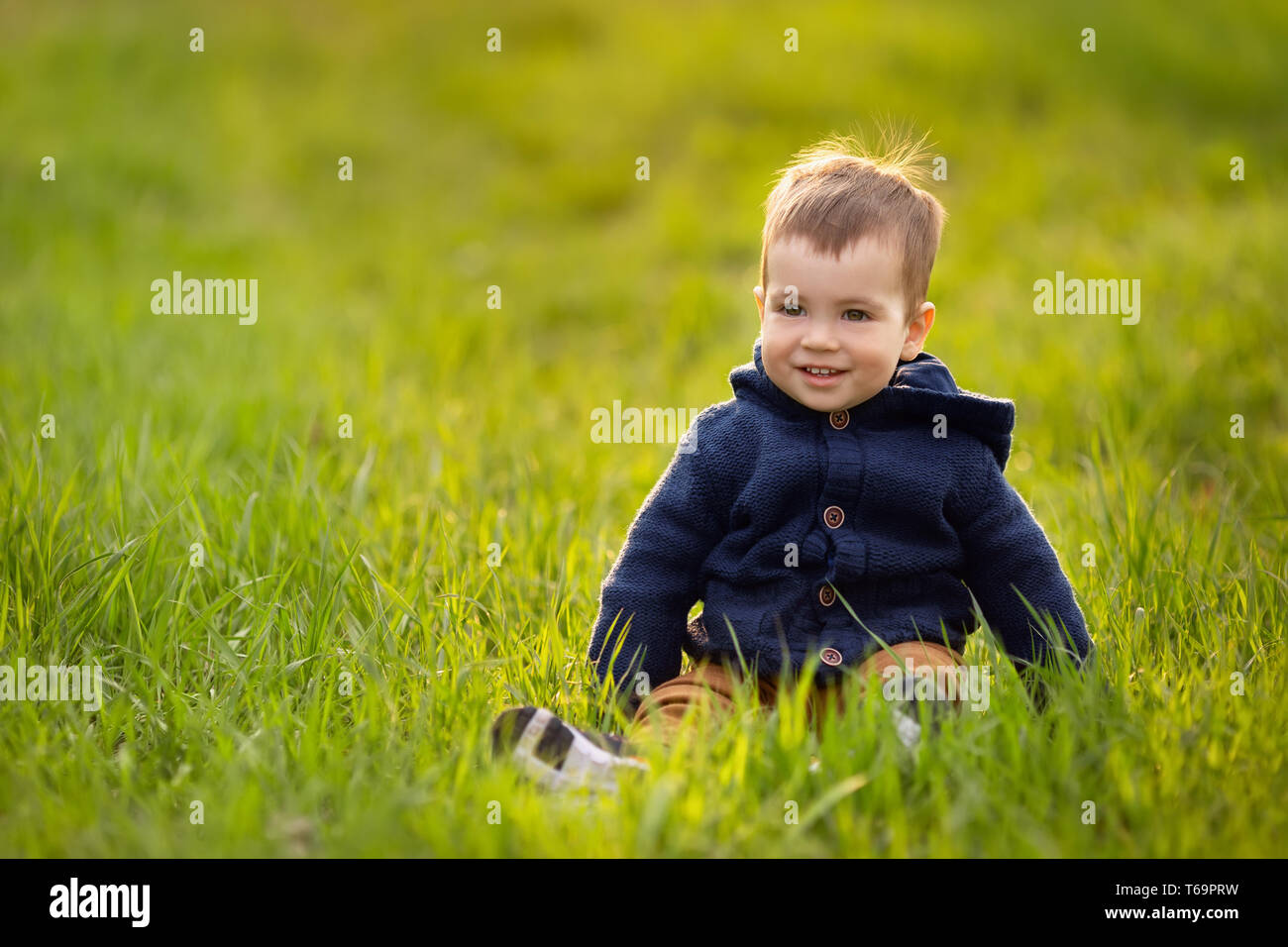 Kleiner Junge in das grüne Gras sitzen Stockfoto