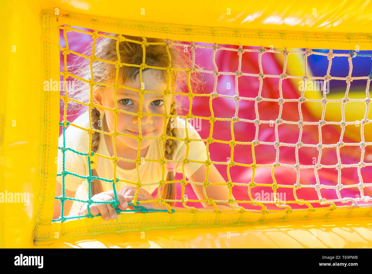 Eine fünfjähriges Mädchen sucht durch ein Netz Trampolin aufblasbar Stockfoto