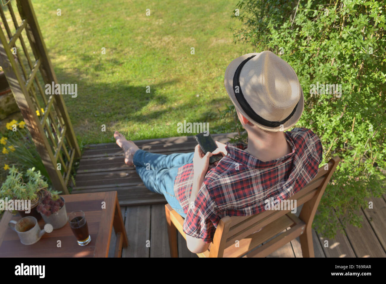 Junger Mann sitzt auf einer Terrasse im Garten mit seinem Smartphone Stockfoto