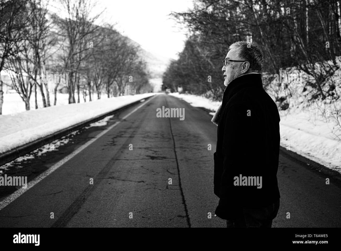 Ein älterer Mann stand auf einer leeren Winter Road, off auf der Seite Stockfoto