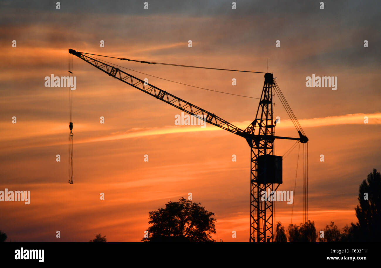 Schwarze Silhouette der ein Baukran bei Dämmerung, Dämmerung und Wolken im Himmel Stockfoto