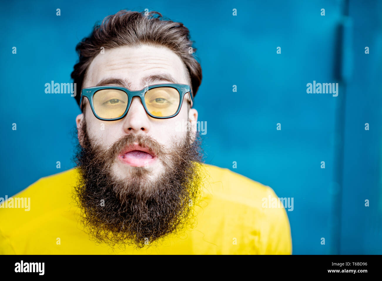 Nahaufnahme Porträt eines verwirrten bärtigen Mann in gelb Pullover und Sonnenbrille auf dem blauen Hintergrund Stockfoto