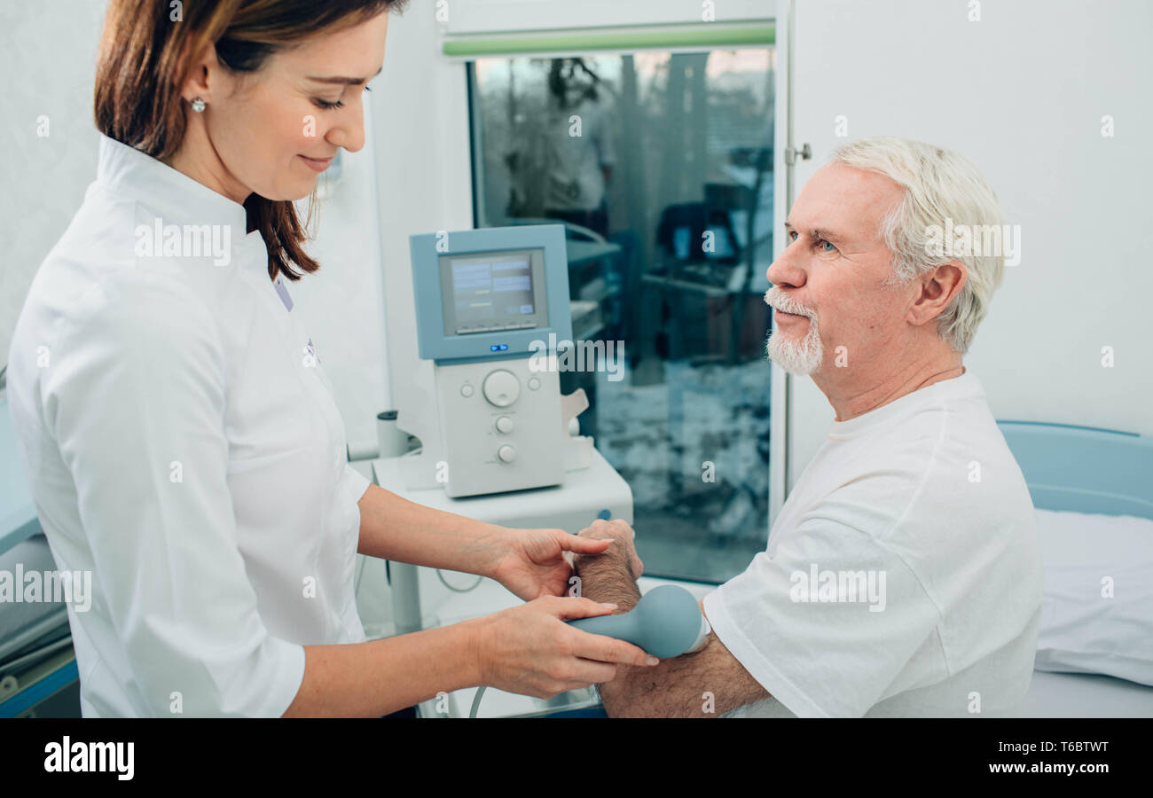 Physiotherapeut mit Ultraschall Maschine an Hand von Client in der Klinik. Physiotherapeutische Behandlung Stockfoto