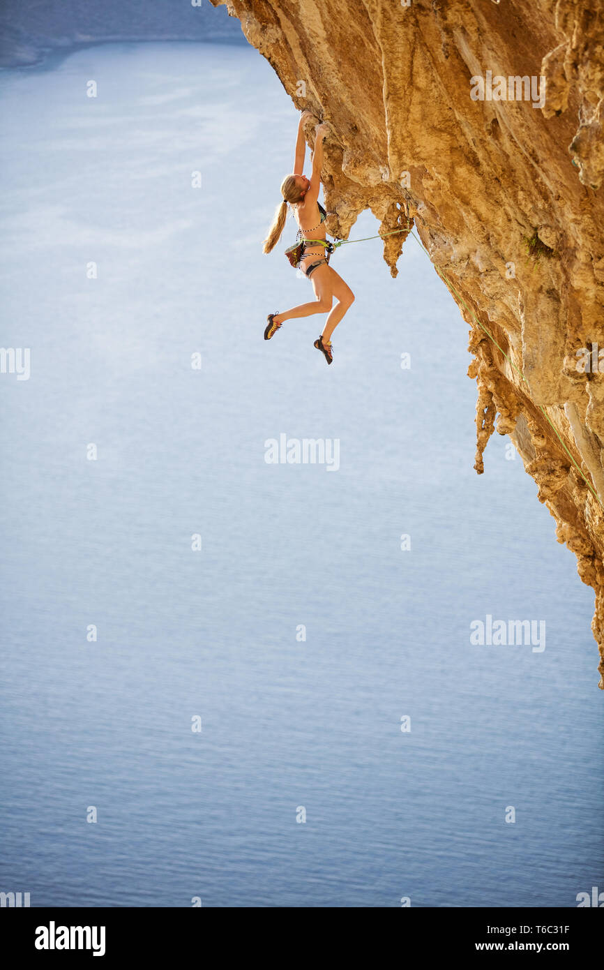 Kaukasische junge Frau im Bikini klettern anspruchsvolle Strecke über Meer Stockfoto