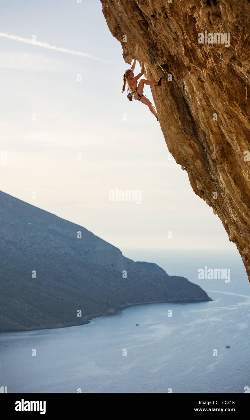 Junge weibliche Kletterer auf anspruchsvolle Route auf überhängenden Felsen über Meer Stockfoto