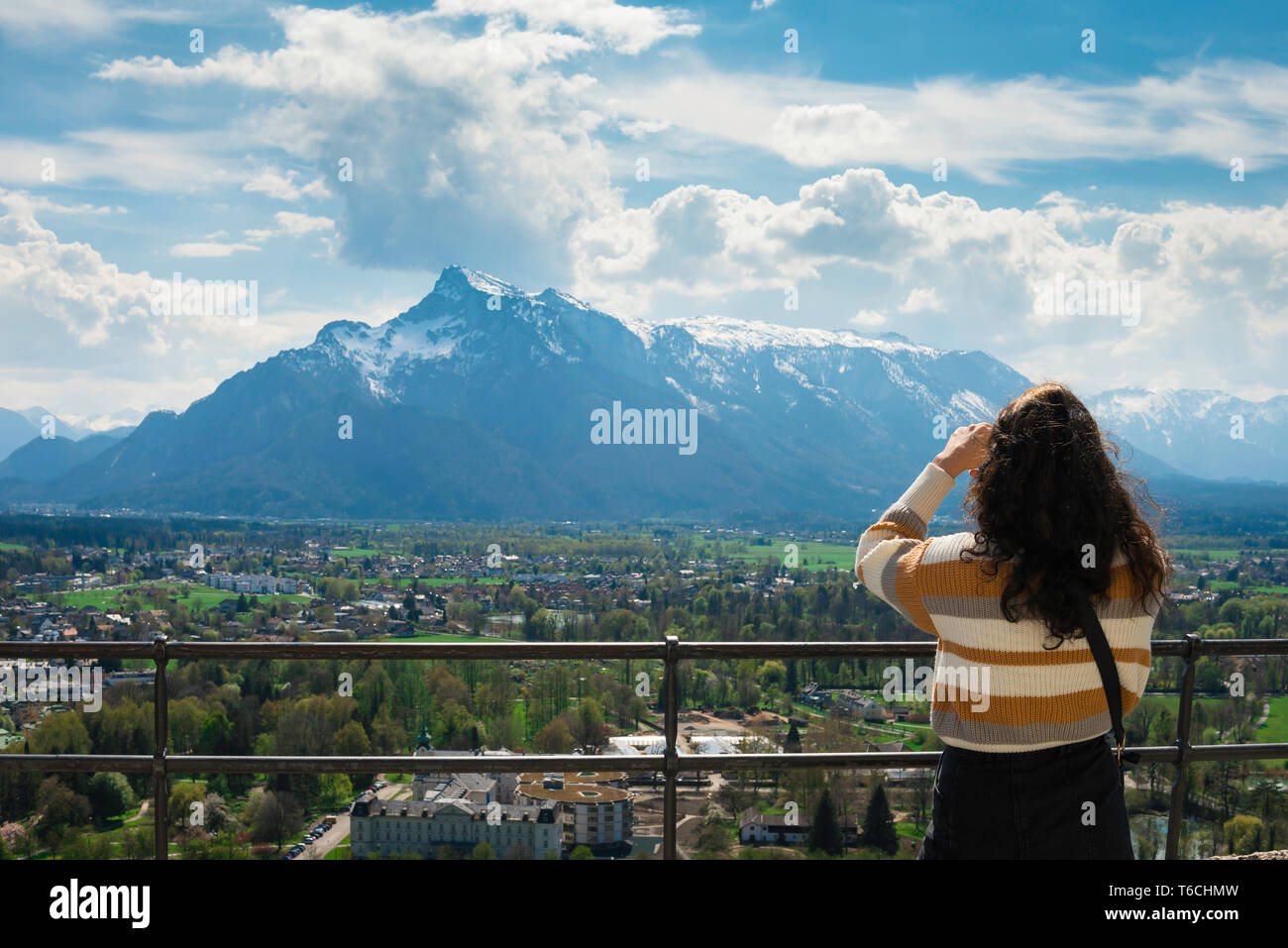 Junge Frau reist, Rückansicht einer jungen Frau, die ein Foto von einer Landzunge-Szene mit alpinen Bergen in Salzburg macht. Stockfoto