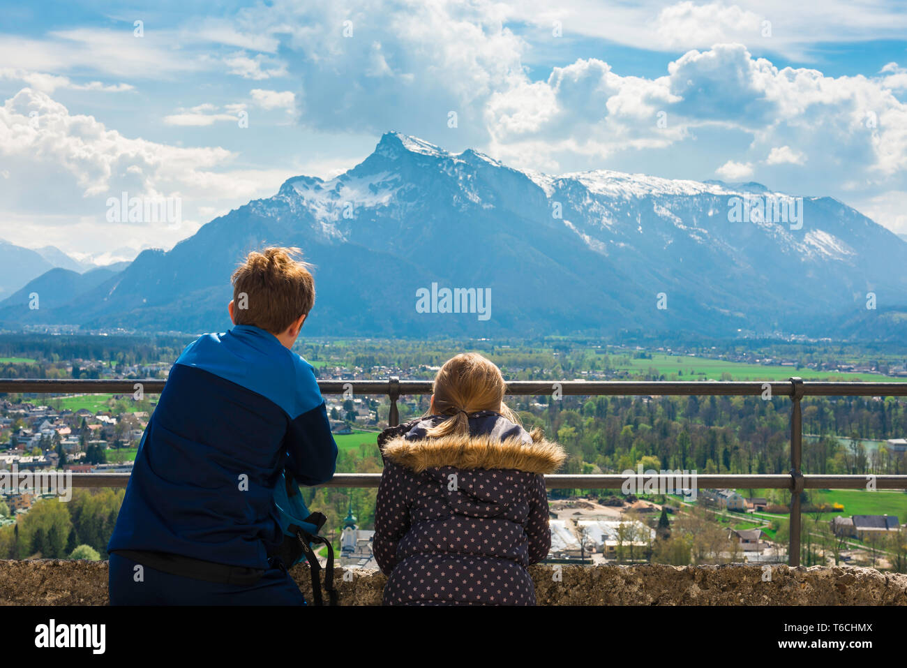 Kinder reisen, Rückansicht der Kinder auf eine alpine Bergwelt von einer Aussichtsterrasse in Salzburg Burg (Festung), Österreich. Stockfoto