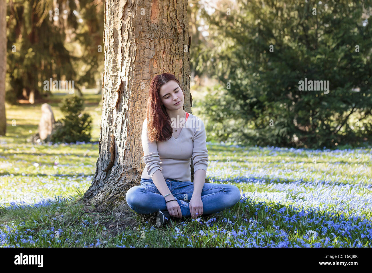 Verträumte junge Frau sitzt in einer Blumenwiese Stockfoto