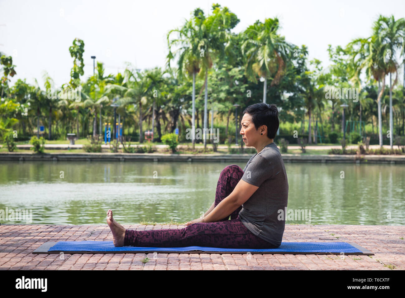 Gesund im mittleren Alter asiatische Frau sitzt mit Knie beim Yoga Übung im Stadtpark am Morgen verbogen. gesund und Lifestyle Konzept. Stockfoto