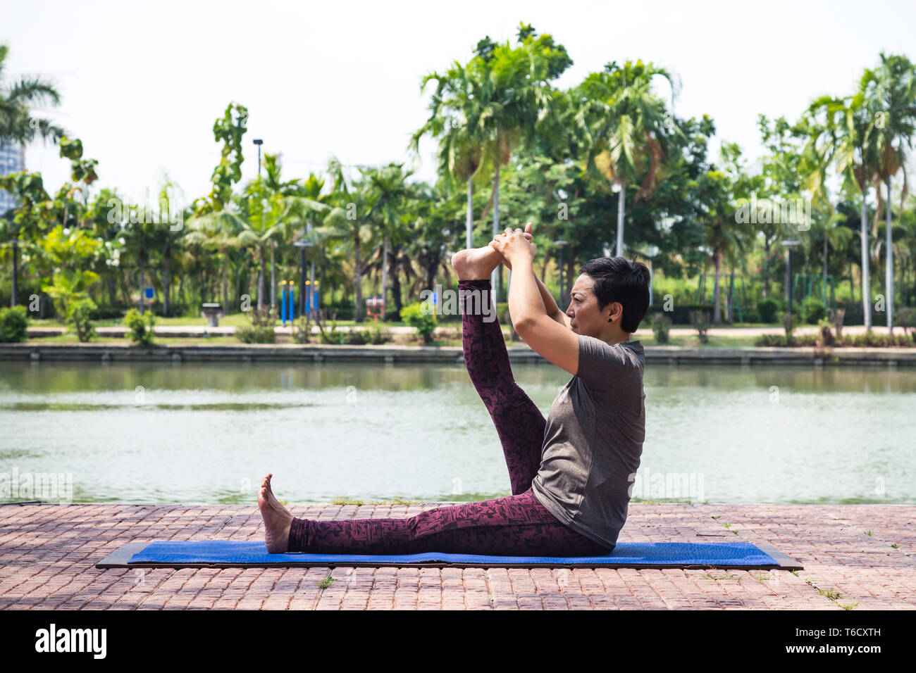 Gesund im mittleren Alter asiatische Frau sitzt auf der Yogamatte mit Yoga Übung im Stadtpark am Morgen. gesund und Lifestyle Konzept. Stockfoto