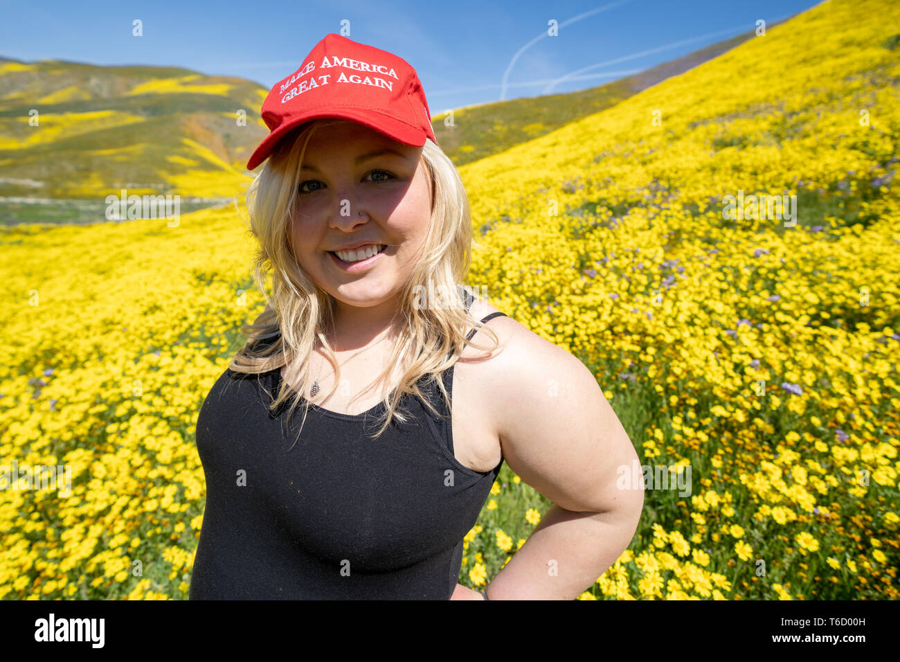 Taft, Kalifornien - 25. März 2019: Blond republikanische Frau trägt ein Donald Trump, Amerika wieder einmal super Hut, stehend in einem Feld von gelben Wildflower Stockfoto