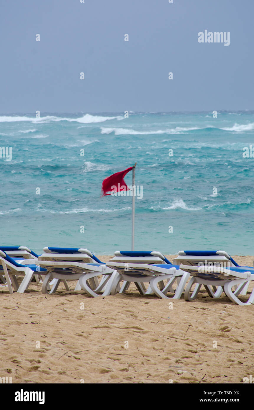 Leere Liegestühle an windigen Strand und Warnung Flagge Stockfoto