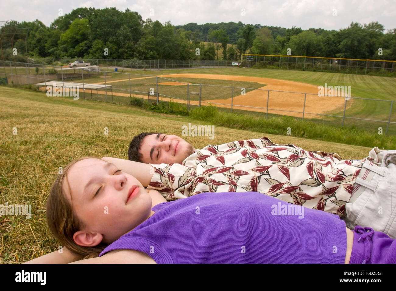 Bruder und Schwester liegend im Gras und Entspannen vor der Baseball Spiel neben einem Baseballfeld. Stockfoto