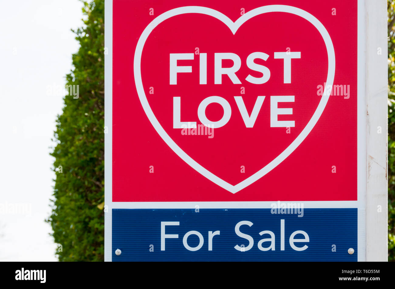 Ein Immobilienmakler Schild an einem Haus für Verkauf liest die erste Liebe in Form eines Herzens. Stockfoto