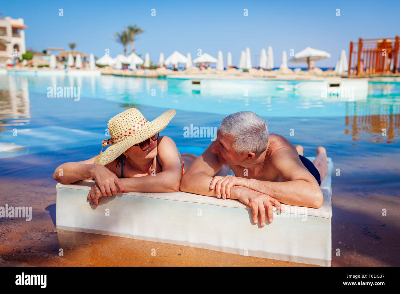 Senior paar Relaxen im Pool liegen auf eine Chaiselongue. Leute genießen Sommer Urlaub. Stockfoto Senior paar Relaxen im Pool liegen auf eine Chaiselongue. Leute genießen Sommer Urlaub. Stockfoto