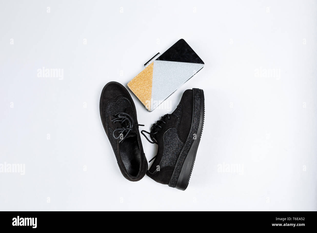 Ein Paar schwarze trendige Schuhe mit glänzenden Einsätzen auf eine dicke Sohle und ein drei-farbe Clutch mit funkelt auf weißem Hintergrund Stockfoto