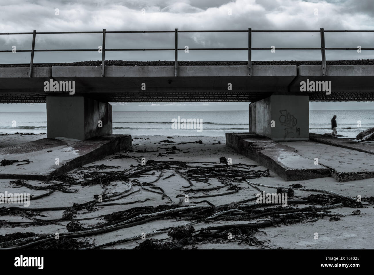 Eine einsame Figur Spaziergänge auf Glencairn Strand vorbei an der Eisenbahnbrücke entlang der False Bay Küste in Südafrikas Western Cape Stockfoto