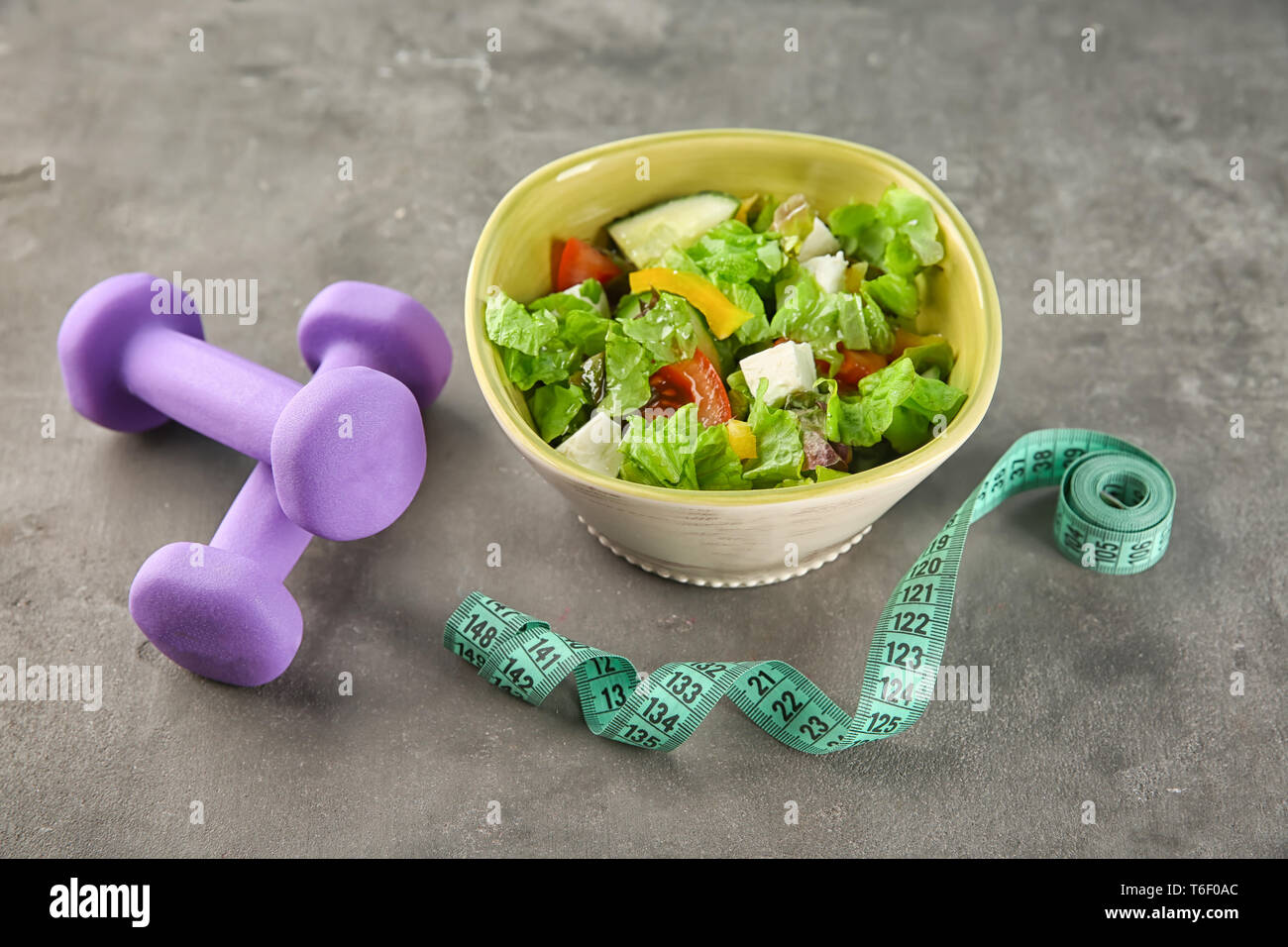 Schüssel mit Salat, Hanteln und Maßband auf Tisch. Ernährung Lebensmittel Stockfoto