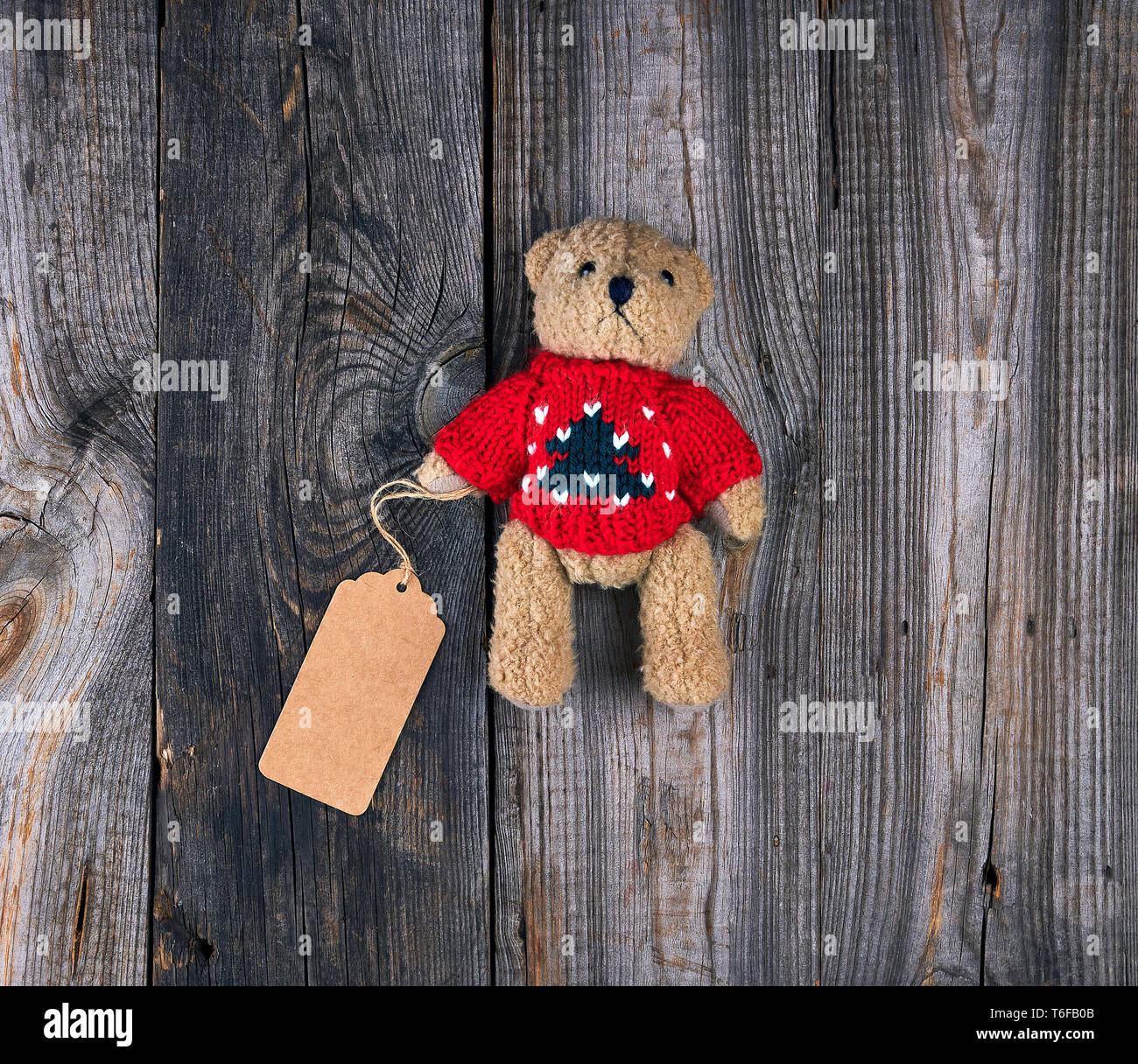 Kleine braune alte Teddybär mit einem Papier leer Tag auf einem grauen Hintergrund Holz, Ansicht von oben Stockfoto