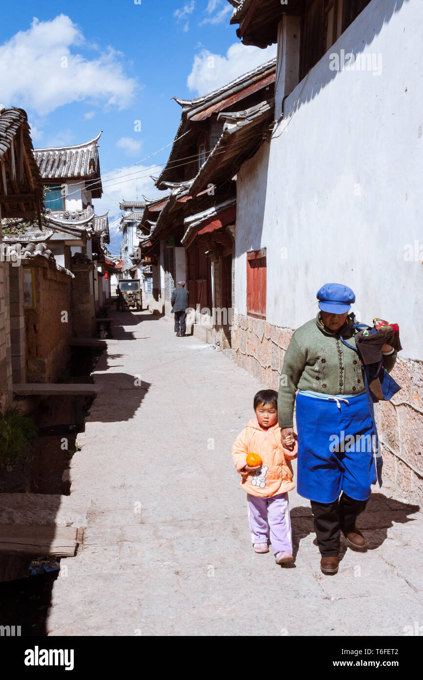 Lijiang, Yunnan, China: eine Frau und ein Kind zu Fuß in eine Gasse in der Altstadt von Lijiang, einem nationalen historischen und kulturellen Stadt zurückgeht. Stockfoto