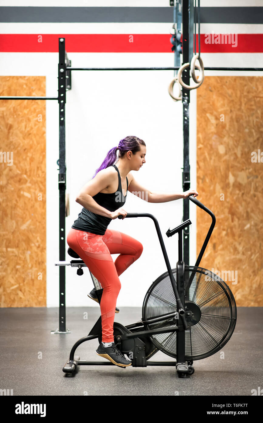 Fit muskulös junge Frau, auf dem Hometrainer in einer Turnhalle in einem aktiven Lebensstil und Gesundheit und Fitness Concept in Seitenansicht Stockfoto