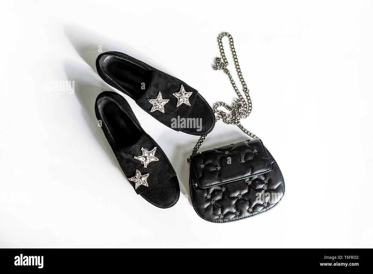Modischer schwarz Leder Schuhe mit Strass stern dekoration und eine schwarze Kupplung auf einer Kette mit Sternen auf weißem Hintergrund Stockfoto