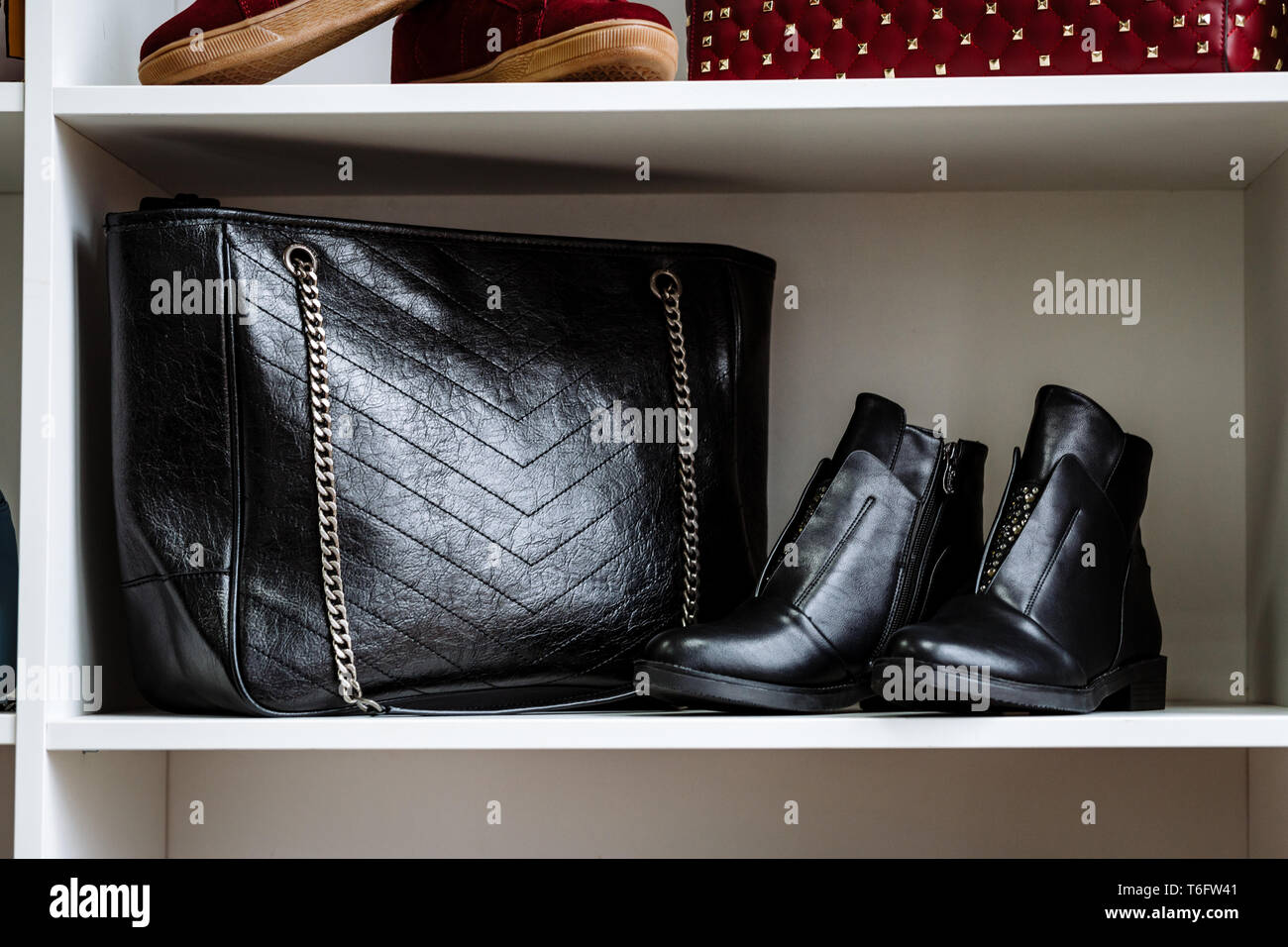 Modische schwarze Schuhe aus Leder mit Strass und eine schwarze Ledertasche auf eine Kette auf ein weißes Regal im Store eingerichtet Stockfoto