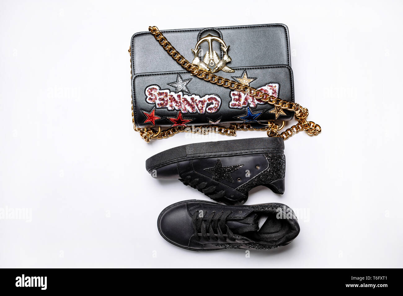 Modische schwarze Sneakers geschmückt mit einem Stern funkelt und eine schwarze Tasche mit einer goldenen Kette geschmückt mit glänzenden Sternen, pailletten Inschrift liebe Cannes Stockfoto