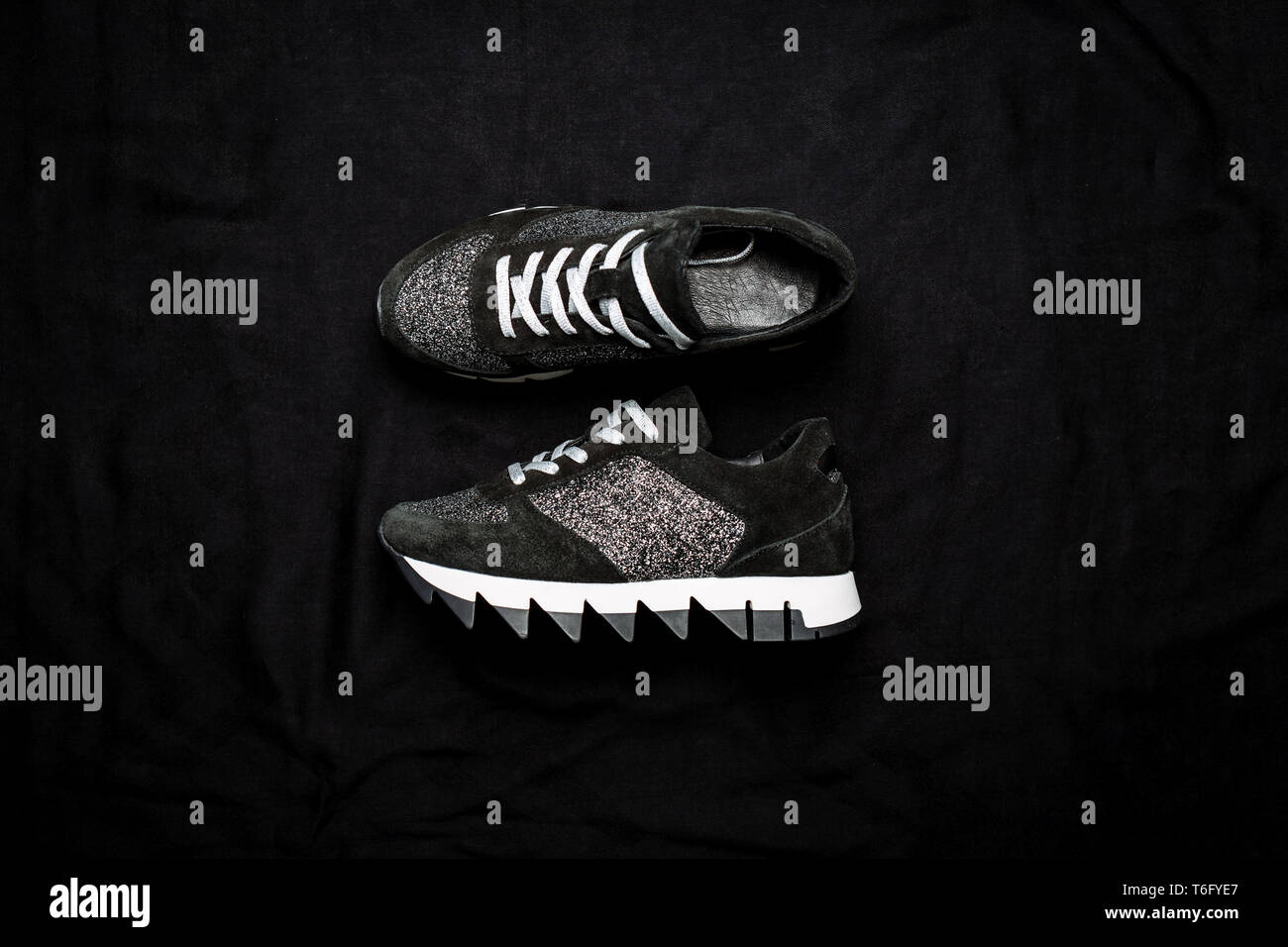 Schwarz Leder Sneakers mit silbernen Pailletten auf einem schwarzen Woven Hintergrund altmodisch eingerichtet Stockfoto