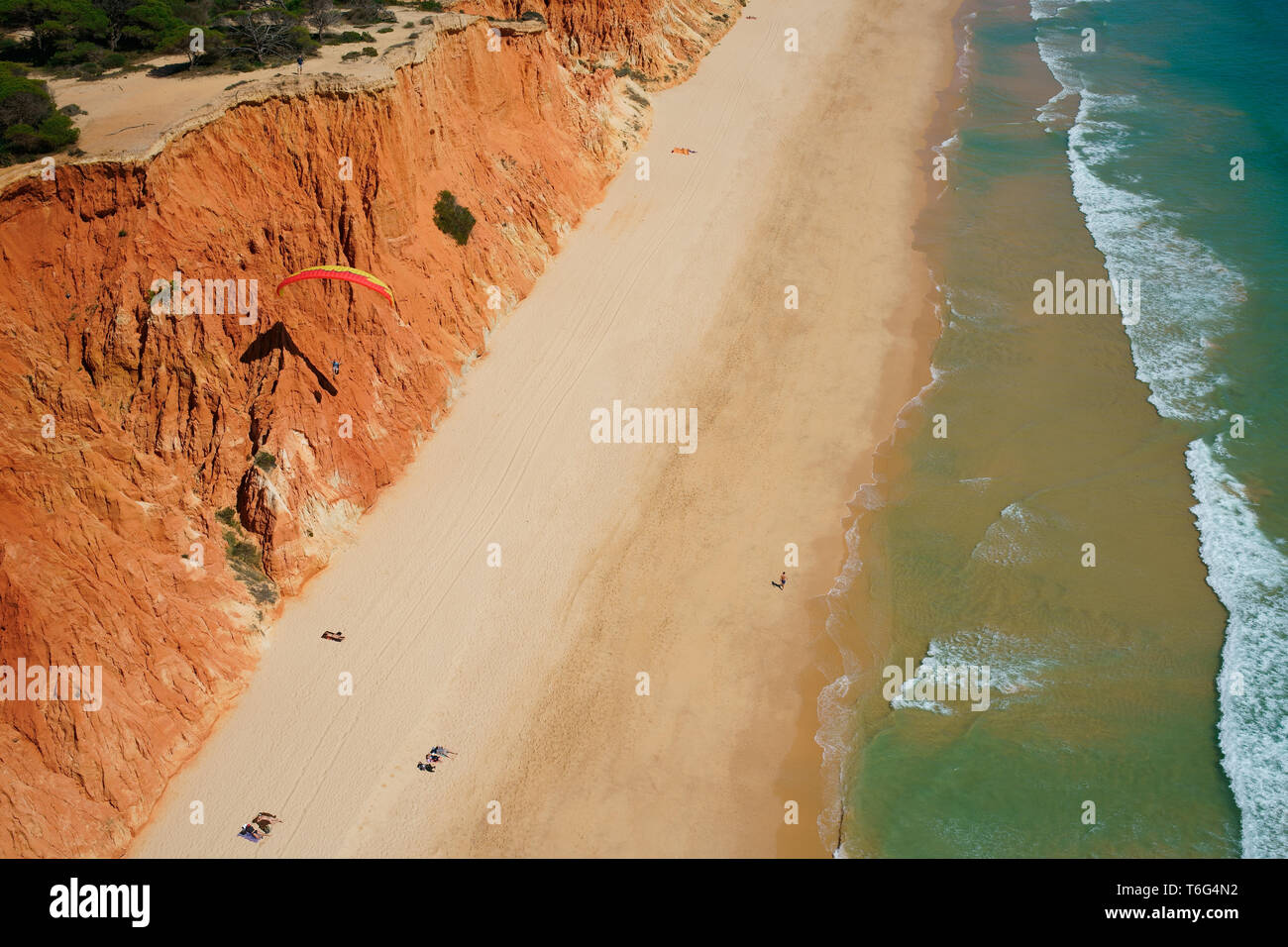 LUFTAUFNAHME. Gleitschirm mit der Meeresbrise, um entlang einer bunten Klippe am Meer zu schweben. Praia da Falésia, Albufeira, Algarve, Portugal. Stockfoto