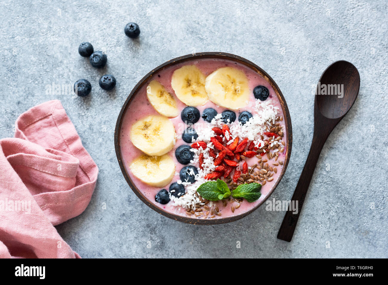 Acai vegan Smoothie Kokosnuss Schale gekrönt mit Banane, Blaubeere, Goji Beeren und Leinsamen. Tabelle Ansicht von oben. Rohkost Stockfoto