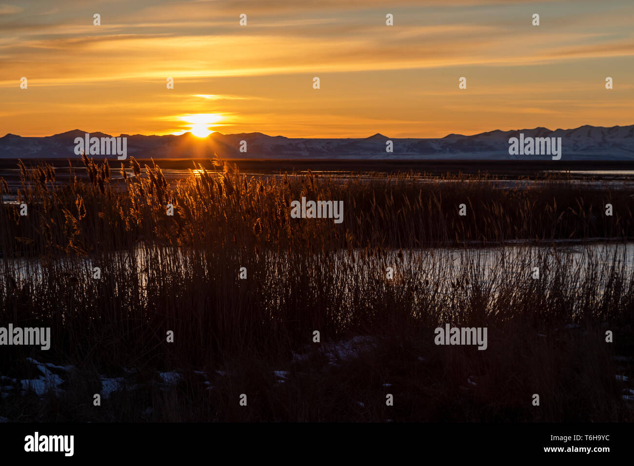 In diesem Schoß die Sonne über dem Vorgebirge Berge wie aus dem Hauptdeich bei Farmington Bay Wasservögel Management Area in der Nähe von Farmington, Utah gesehen. Stockfoto